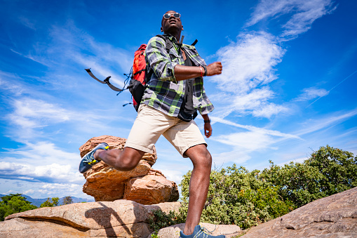 Young african american jumping trekking in mountain peak with backpack