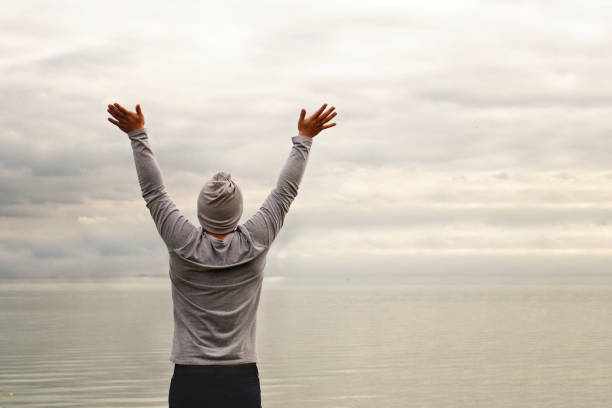 istock A young man is standing on the shore. The view from the back. Yoga classes. Hands raised up. Freedom and achievement. 1178666127