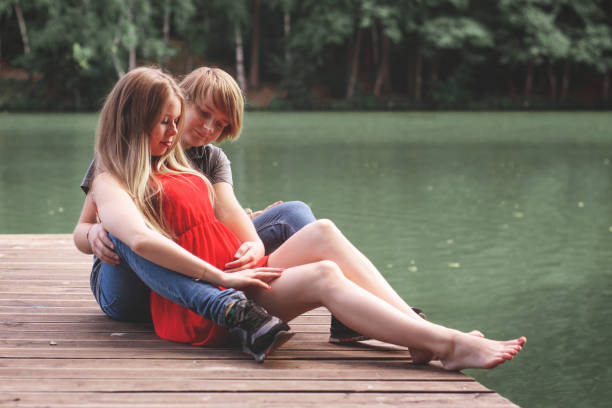 A happy married couple Husband hugs a beautiful adult pregnant wife. walks in a park by the lake. Second trimester. Holds her hands on her stomach. The benefits of walking during pregnancy, health care una feliz pareja casada marido abraza a una hermosa esposa embarazada adulta. camina en un parque junto al lago. segundo trimestre. sostiene sus manos sobre su estómago. los beneficios de caminar durante el embarazo, el cuidado de la salud.