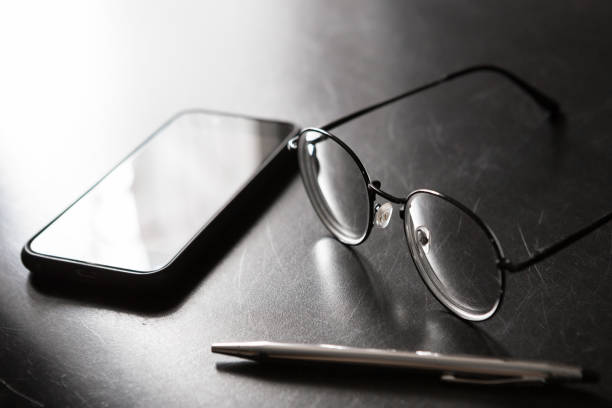 Selective focus of Pen, glasses,  smartphone on black background and copy space with light and shadow