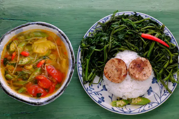 Plate of rice dish with boiled water morning glory, vegan sausage cook with sauce and sour soup bowl from tomato, okra, pineapple, a nutrition and delicious vegetarian meal for serving lunch