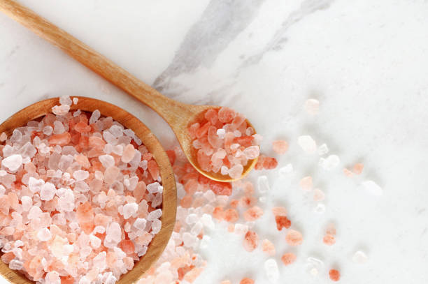 top view of himalayan pink rock salt in wooden bowl and spoon on white marble table. top view of himalayan pink rock salt in wooden bowl and spoon on white marble table. himalayas stock pictures, royalty-free photos & images