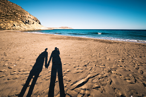 Shadows of young couple holding hands on Playa del Plomo (Andalusia, Spain).