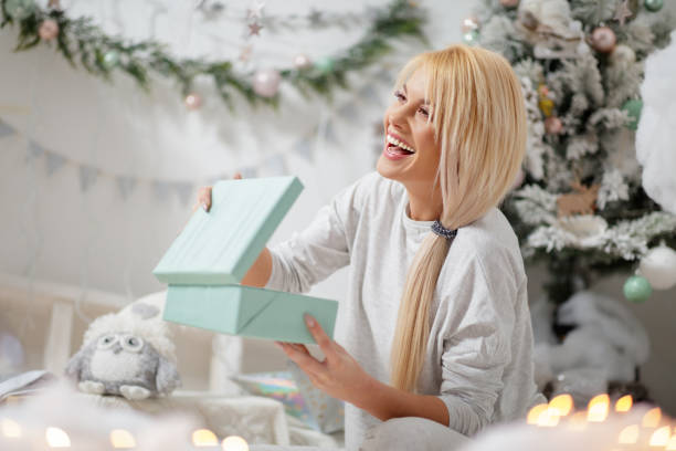 mujer feliz en pijama sosteniendo regalo por el árbol de navidad - beautiful women gift christmas fotografías e imágenes de stock