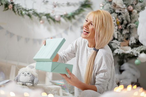 Woman in pajamas holding gift box pleased with her Christmas present