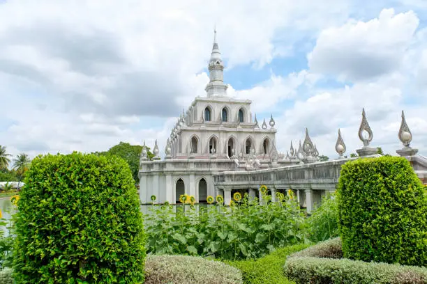 Photo of The symbolic building of Sukhothai Thammathirat Open University,the traditional Thai style pavillion stand on the pond or lake,sunflower in front with green bush in round shape, Nonthaburi, Thailand.