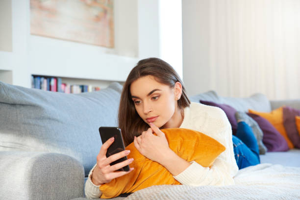 istock Smiling young woman text messaging while relaxing on sofa at home 1178720911