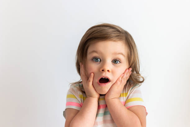 surpris enfant en bas âge choqué avec ses mains sur des joues et les yeux bleus grands ouverts. verticale de chéri dans la surprise - surprise child little girls shock photos et images de collection