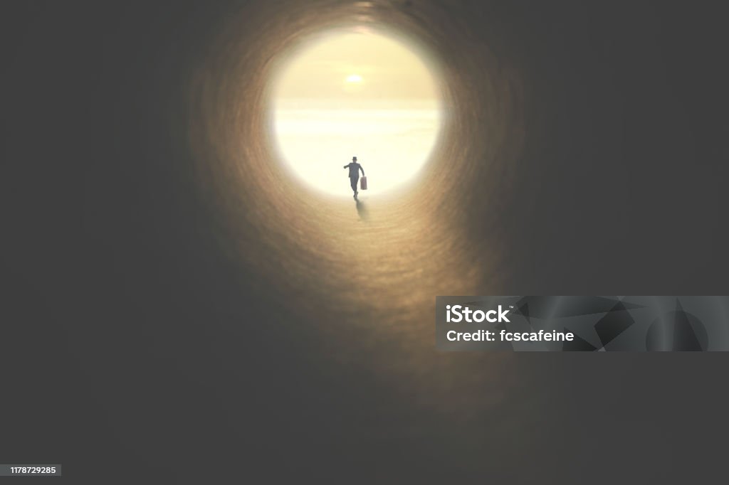 man with suitcase running to the exit of a tunnel illuminated of the sun Escaping Stock Photo