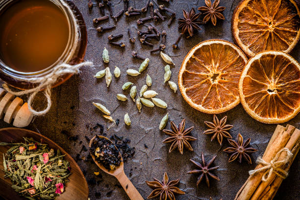 Aromatic spices with copy space on a dark textured backdrop Top view of various kinds of aromatic spices like cinnamon sticks, star anise, cardamom, cloves and dried sliced oranges. At the left side are two kinds of dried tea leaves and a honey jar with a honey dipper. Objects are on a dark textured backdrop. Low key DSLR photo taken with Canon EOS 6D Mark II and Canon EF 24-105 mm f/4L star anise stock pictures, royalty-free photos & images