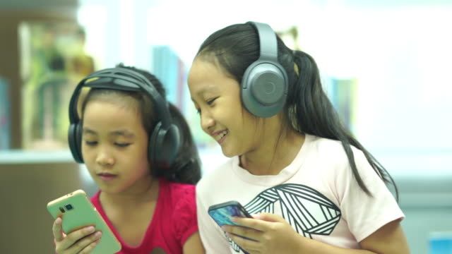 Two Asian girls singing and listening music from headphones