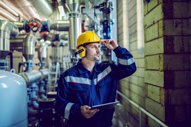 istock Dedicated plant worker in working clothes, with helmet on head and antiphons on ears posing with tablet in hands. 1178739533