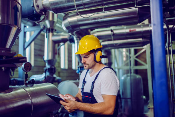 istock Focused plant worker in overalls, with protective helmet on head and antiphons on ears using tablet for checking machine. 1178740002