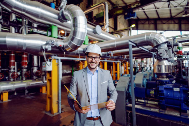 istock Handsome caucasian businessman in suit and with protective helmet on head holding folder with documents and looking at camera while standing in power plant. 1178741025