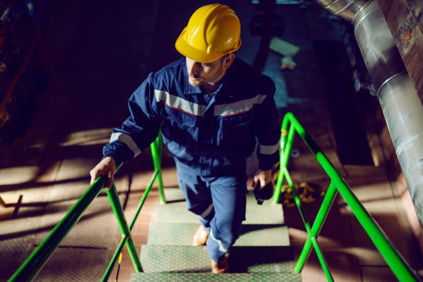 Full length of caucasian worker dressed in blue work suit and with protective helmet on head climbing up the stairs. Energy plant interior. Full length of caucasian worker dressed in blue work suit and with protective helmet on head climbing up the stairs. Energy plant interior. caution step stock pictures, royalty-free photos & images