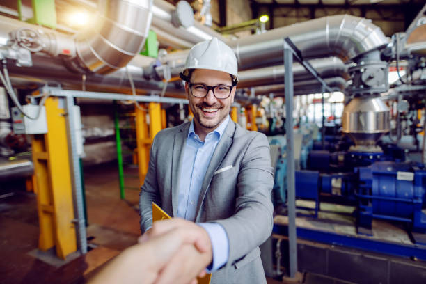istock Handsome caucasian manager in suit and with helmet on head holding folder with documents and shaking hands with investor while standing in power plant. 1178741412