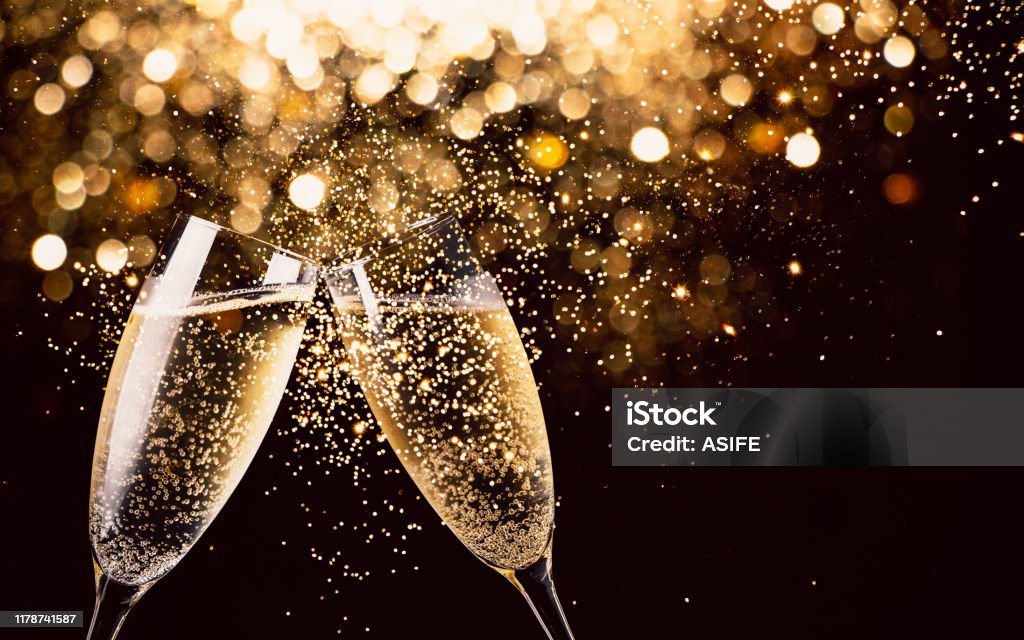 Celebration toast with champagne Two glasses of champagne toasting in the nigh with lights bokeh, glitter and sparks on the background Champagne Stock Photo