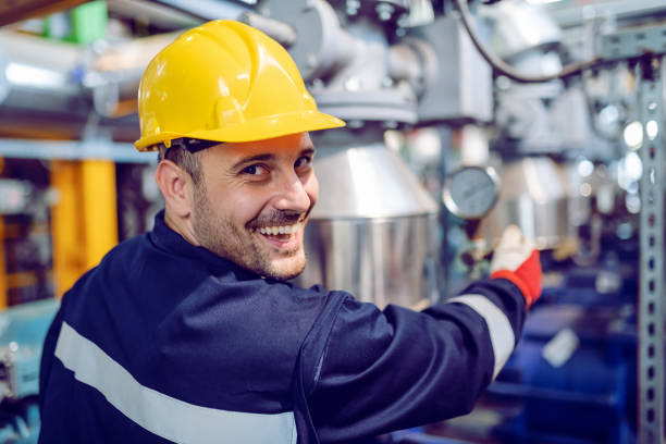 trabajador sonriente de la planta de energía trabajadora en la válvula de tornillo traje de trabajo mientras mira la cámara. - boiler power station fuel and power generation gas boiler fotografías e imágenes de stock