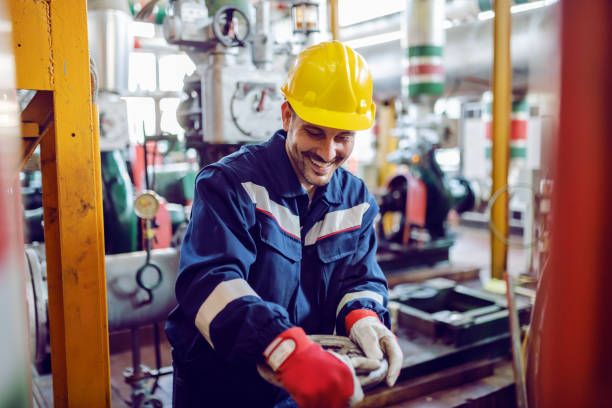 trabajador sonriente de la planta de energía trabajadora en la válvula de atornillado de traje de trabajo. - boiler power station fuel and power generation gas boiler fotografías e imágenes de stock