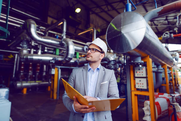 istock Handsome caucasian businessman in suit and with protective helmet on head holding folder with documents while standing in power plant. 1178743039