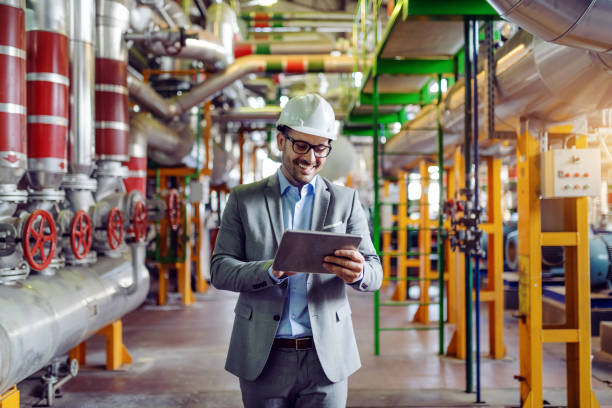 istock Handsome caucasian manager in gray suit and with helmet on head using tablet and walking. Power plant interior. 1178743788