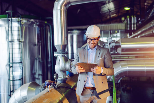 istock Handsome smiling caucasian supervisor in suit and with helmet on head using tablet while standing in power plant. 1178743833