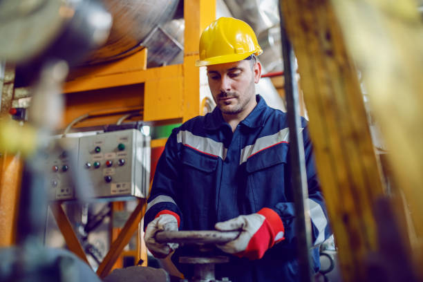 istock Hardworking energy plant worker in working suit and with protective helmet on head screwing valve. 1178743906