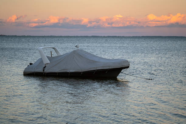 barca coperta attraccata al molo vicino alla riva al tramonto. yacht coperto sull'acqua con colorato cielo al tramonto sullo sfondo - beach rope nautical vessel harbor foto e immagini stock