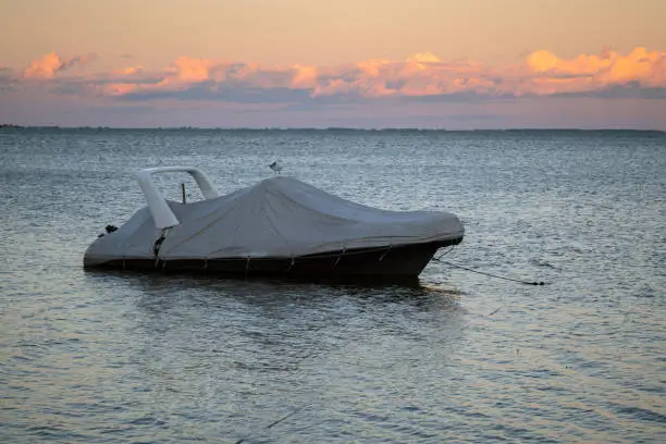 Photo of Covered boat docked at the pier by the shore at sunset. Covered yacht on the water with colourful sunset sky in the background