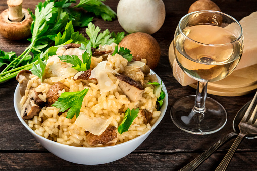 Risotto ai funghi, mushroom rice, with ingredients and a glass of white wine on a dark rustic wooden background