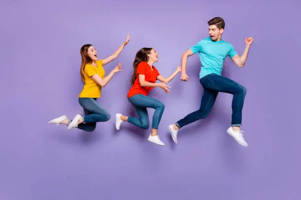 Photo of Full size body side profile view photo of one unhappy shocked guy running away from two obsessive addicted ladies isolated violet background
