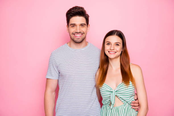 portrait of charming married people with long haircut smiling cuddling wearing striped t-shirt dress isolated over pink background - long hair red hair women men imagens e fotografias de stock