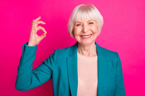 Close-up portrait of nice attractive lovely cheerful cheery content gray-haired lady wearing, blue jacket showing ok-sign ad advert isolated on bright vivid shine vibrant pink fuchsia color background