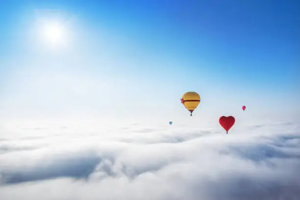 Yellow and red balloons in the blue sky over white clouds and the sun
