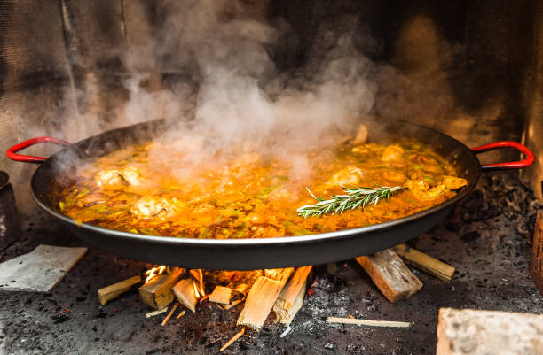 Cooking and making a traditional Spanish Paella over open fire. Traditional way of preparing Valencian paella  with fire wood and flames in a big pan. Made from Chicken and Rabbit meat in fireplace.