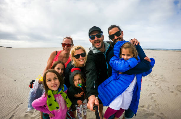 ビーチに立つ家族や友人のグループは、自分撮りを取ります。 - people child twin smiling ストックフォトと画像