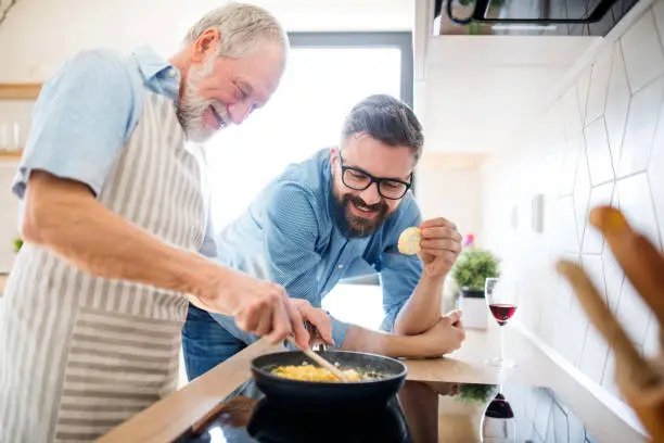 Photo of An adult hipster son and senior father indoors at home, cooking.