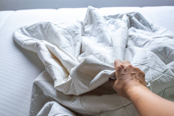 istock Woman's hand picking up white crumpled bed sheet on white bed, Close up shot, Selective focus, Bedroom cleaning concept 1178761433