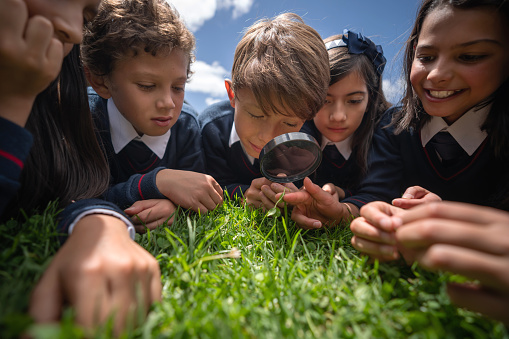 Group of kids in science class outdoors looking at the grass through a magnifying mirror â education concepts