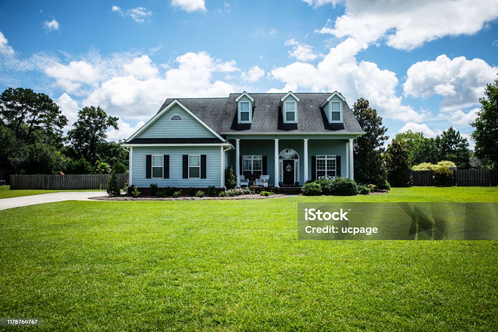 Front View of blue house with siding in the suburbs pale blue house with siding on a large lot with traditional windows and shutters in a subdivision in the suburbs on a bright sunny blue sky day House Stock Photo