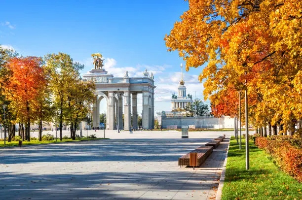 View of the Main Entrance and the Central Pavilion of VDNH in Moscow from a park with trees with autumn yellow-red foliage