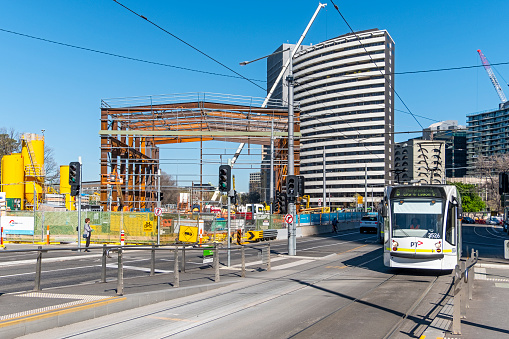 Melbourne, Australia; Oct 1, 2019: Victoria's Big Build: Metro Tunnel construction site for Anzac Station and Domain train-tram interchange on busy St Kilda Road showing construction of huge acoustic shed with city office buildings in the background and PTV tram heading to the Melbourne CBD