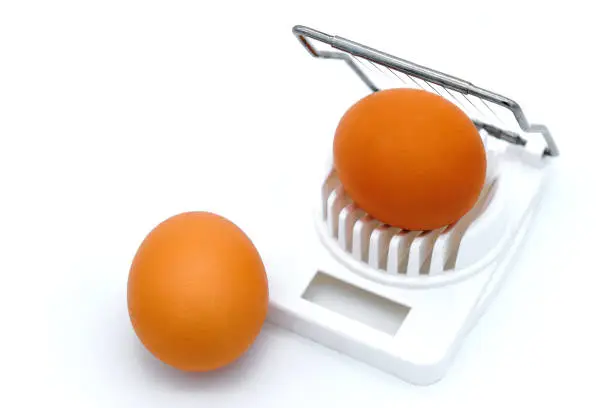 White background, isolate. White egg-cutter close-up. Orange egg in shell and cutter.