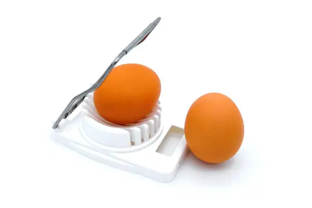 Orange egg in a white egg-cutter. White background, isolate. Kitchen equipment for cutter eggs.