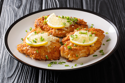 Traditional tasty cheese Romano chicken breast fried breaded served with lemon and green onion closeup on a plate on the table. horizontal