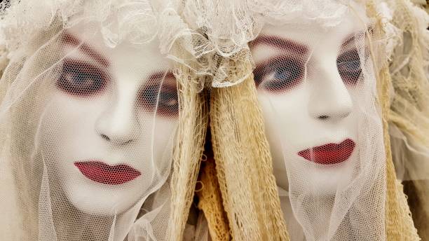 Two ghoulish undead bride Halloween decorations. Two female zombie bride mannequins with faces painted white, wearing makeup and lace veils for Halloween. Focus is on their faces filling the frame. scary bride stock pictures, royalty-free photos & images