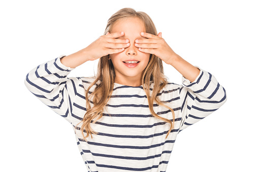 front view of smiling kid covering eyes with hands isolated on white