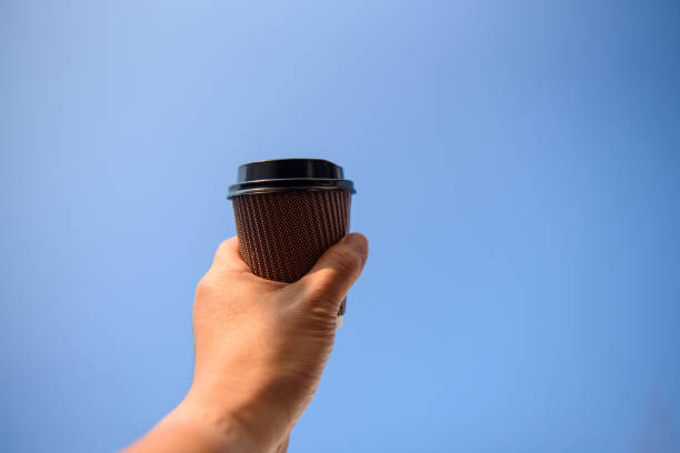 istock Man hand holding paper cup in the blue sky 1178779687