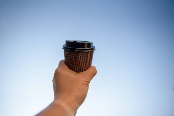 istock Man hand holding paper cup in the blue sky 1178779711