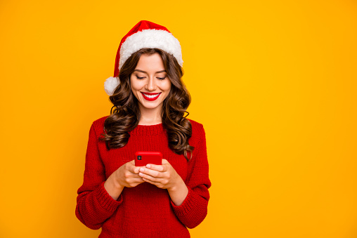 Photo of amazing lady holding telephone in hands wear knitted pullover and santa, hat isolated yellow background